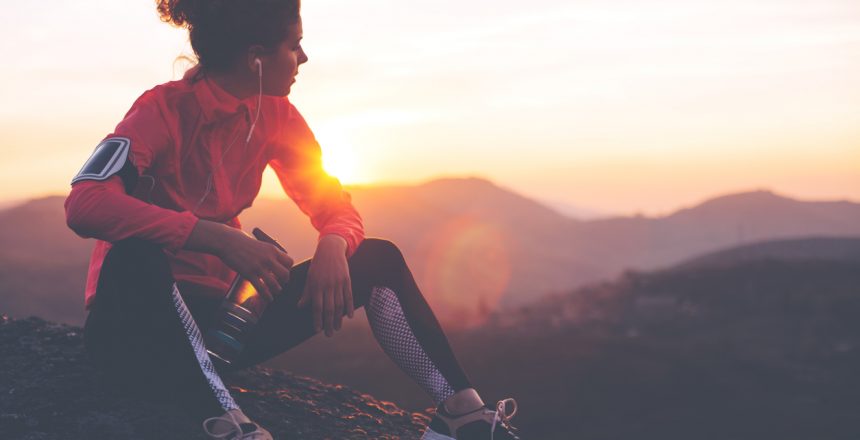 Athletic woman resting after a hard training in the mountains at sunset. Sport tight clothes.